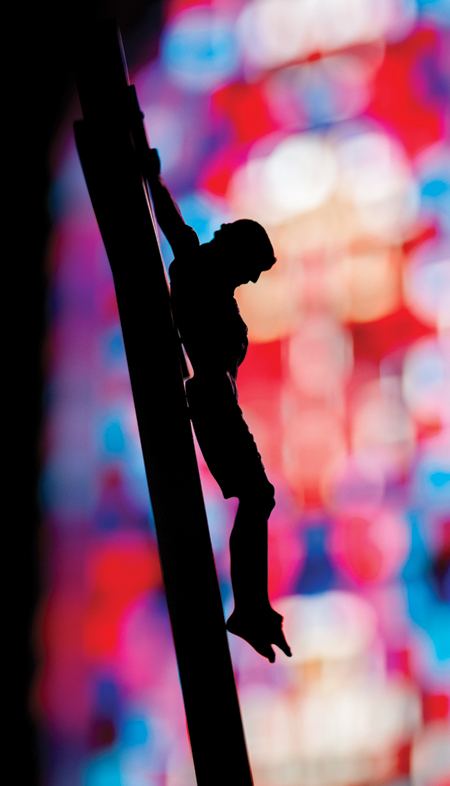 A crucifix is silhouetted against a stained-glass window at the chapel inside Elmira Correctional Facility, a maximum security prison in Elmira, N.Y. March 18. Good Friday, observed April 18 this year, commemorates the passion and death of Jesus. (CNS photo/Mike Crupi, Catholic Courier) (March 20, 2014)