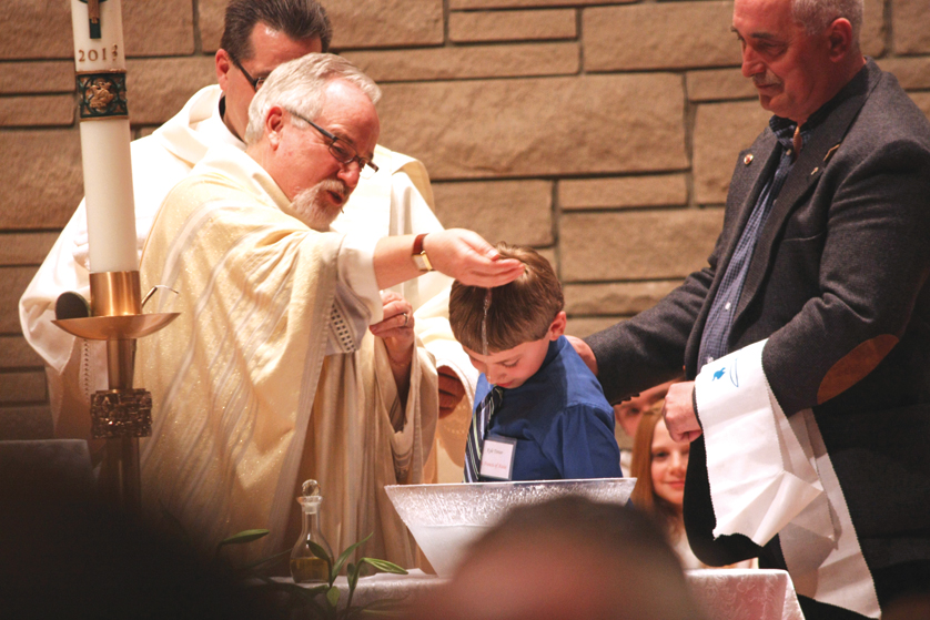 Fr. Lawrence Delonnay, pastor of Our Lady of the Lakes Parish in Waterford, baptizes a boy during the Easter Vigil in 2013. 