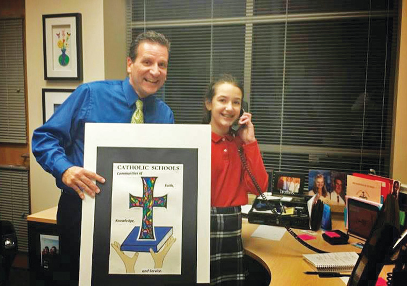 Emma Sarkisian, a sixth-grader at Holy Family Regional School in Rochester, calls her mother as Principal Jon Myers displays Emma’s winning poster in the Archdiocese of Detroit’s Catholic Schools Week poster contest. Emma’s poster tied with Charles Freese, a fifth-grader from Immaculate Conception School in Ira Township, for first place in the elementary school contest, and Marine City Cardinal Mooney’s Monica Freeman won first place in the high school contest. The winners’ designs will be distributed and hung in schools across the archdiocese during Catholic Schools Week, which is Jan. 25-31. Posters highlighted the Catholic Schools Week theme of “Communities of Faith, Knowledge and Service.” The winners also earned $500 for their schools and will receive a professionally framed edition of their posters. 