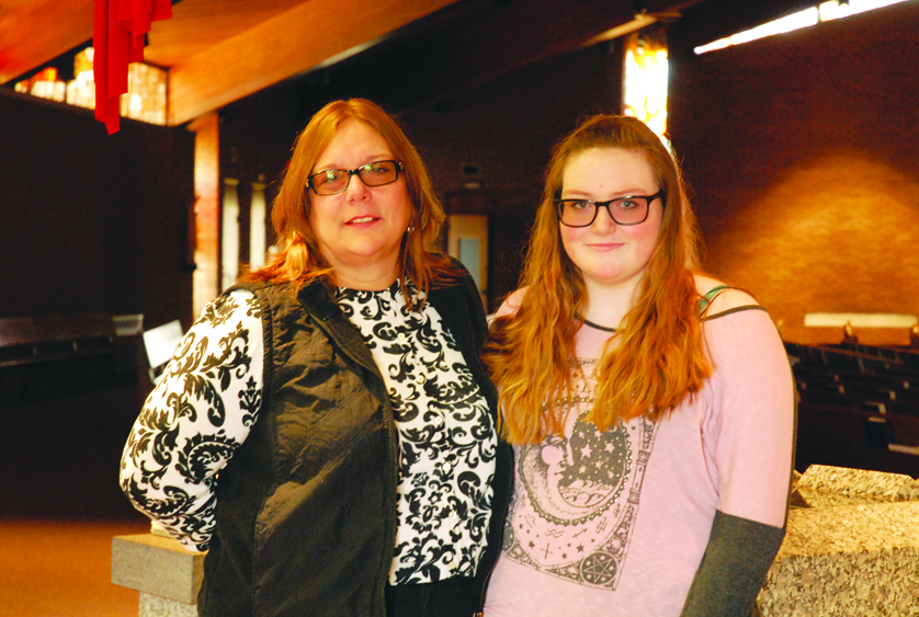 Kitty Moore, left, and her daughter, Ciara Moore, stand before the baptismal font at St. Martin de Porres Parish in Warren, where Ciara will be baptized at tomorrow’s Easter Vigil. Kitty Moore will receive the rest of her sacraments that day, too. 