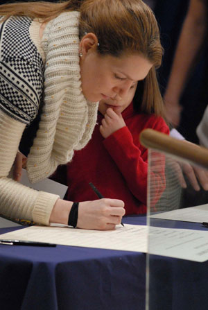 A catechumen signs the Book of the Elect as a little girl looks on Feb. 21.