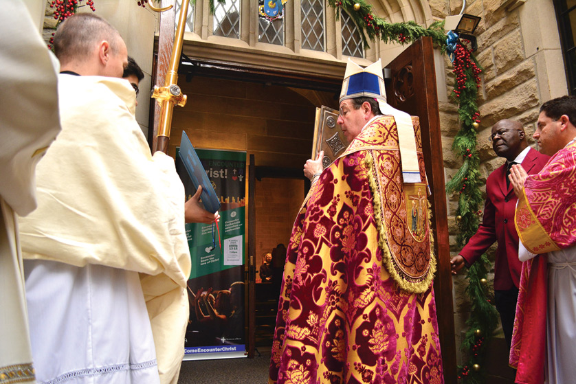 Archbishop Allen H. Vigneron holds the Book of the Gospels as he processes through the Holy Door at the Cathedral of the Most Blessed Sacrament on Dec. 13. The opening of the Holy Door also marks the beginning of the extraordinary Jubilee Year of Mercy for the Archdiocese of Detroit, which will continue until the feast of Christ the King on Nov. 20, 2016 and the end of the Archdiocesan Synod on Evangelization. Mike Stechschulte | The Michigan Catholic