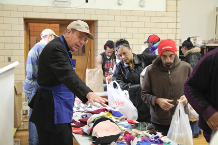Archbishop Allen H. Vigneron helps hand out hats, gloves and scarves at the Matchan Nutrition Center in Pontiac on Dec. 22. The soup kitchen, which serves hot meals to approximately 500 people every Tuesday and Thursday, is in the gym of St. Vincent de Paul Church, part of St. Damien of Molokai Parish. Photos by Jonathan Francis | Archdiocese of Detroit