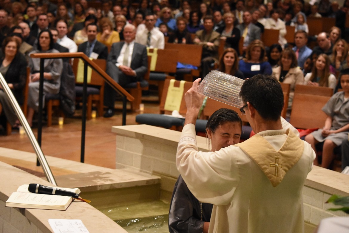 Fr. John Riccardo baptizes a new Catholic as the faithful look on at Our Lady of Good Counsel Parish in Plymouth during the Easter Vigil. (Dan Meloy | The Michigan Catholic)