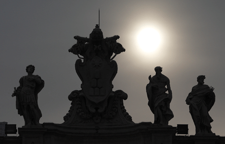 A papal tiara and keys are silhouetted between saints o the colonmade as the sun shins from behind clouds in the morning in St. Peter's Square at the Vatican. Paul Haring|CNS Photo