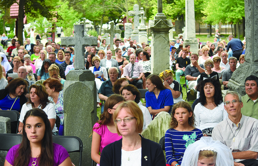Massgoers sit among the gravestones in the cemetery at Assumption Grotto during the Mass.