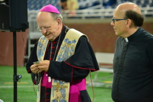 Bishop Francis R. Reiss leads the rosary from the 50-yard line of Ford Field during the kickoff prayer service for the CHSL's 90th season.