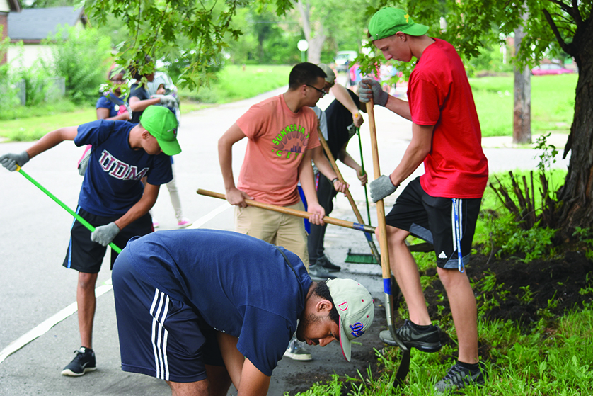 University of Detroit Mercy freshmen dig up weeds and shovel dirt as part of a neighborhood cleanup project during the university’s student orientation.
