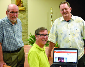 Left to right, Dr. Robert Halpert, Bill Griffin and Tim Schwab hold a computer open to their website, Wtness.org, which they created to collect and share stories of God’s working in ordinary people’s lives.