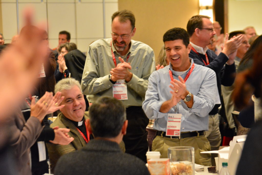 Synod members clap and cheer in a round of applause for priests during the fourth and final session of Synod 16, on Archdiocesan Central Services, on Nov. 20. Sitting is Fr. Chris Talbot, pastor of St. Francis of Assisi-St. Maximilian Kolbe Parish in Ray Township. (Mike Stechschulte, The Michigan Catholic)
